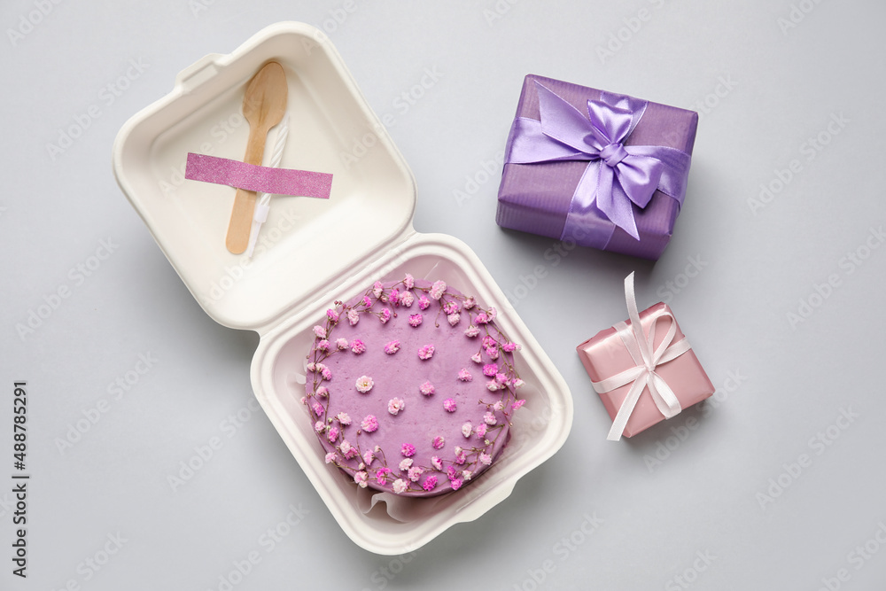 Plastic lunch box with tasty bento cake and gifts on grey background Plastic lunch box with tasty bento cake and gifts on grey background