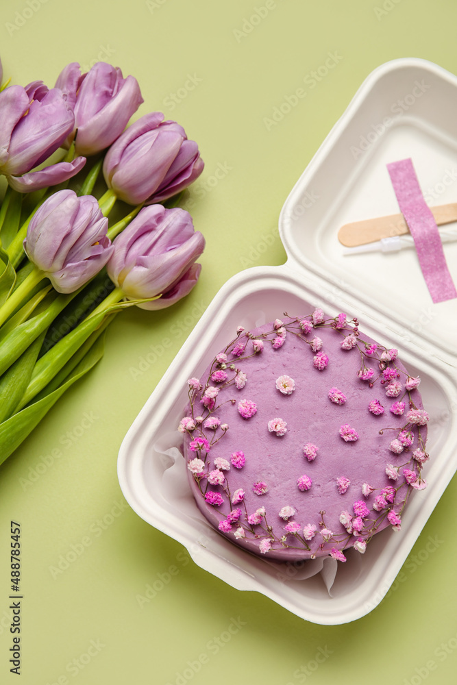 Plastic lunch box with tasty bento cake and flowers on green background Plastic lunch box with tasty bento cake and flowers on green background
