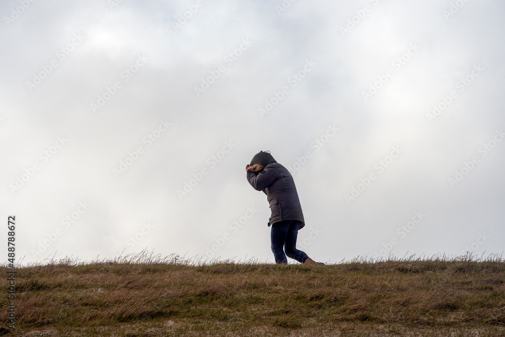 A man walks against the storm and protects his face from the strong wind A man walks against the storm and protects his face from the strong wind