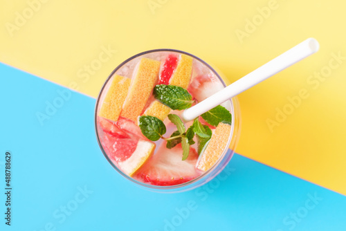 Glass with fruit iced tea drink in blue and yellow backgrounds top view.
