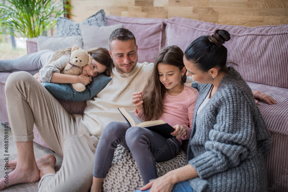 Two happy sisters with mother and father sitting on floor hugging and reading book at home Two happy sisters with mother and father sitting on floor hugging and reading book at home