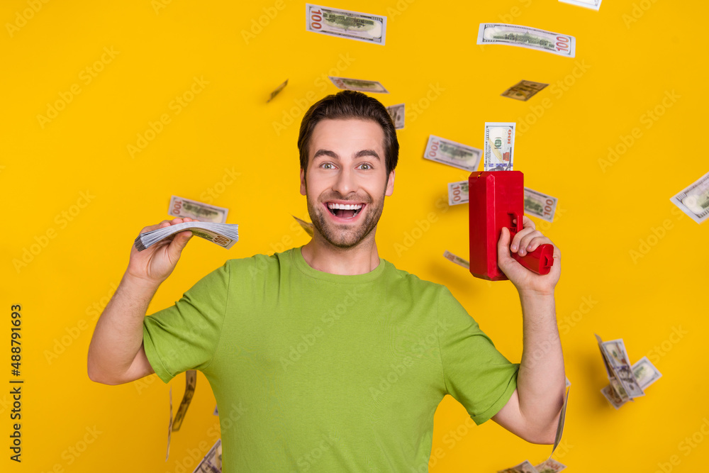 Photo of cool beard young guy hold money gun wear green t-shirt isolated on yellow color background Photo of cool beard young guy hold money gun wear green t-shirt isolated on yellow color background
