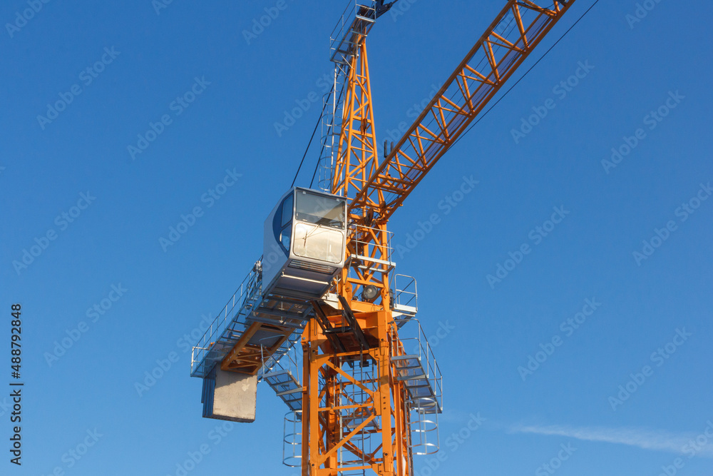Tower crane against the blue sky. Tower crane operator's cabin. Crane operator at work. Tower crane against the blue sky. Tower crane operator's cabin. Crane operator at work.