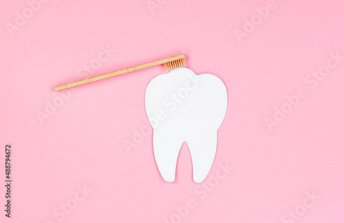 Dental care concept, copy space. White tooth and wooden toothbrush on a pink background.