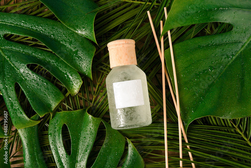 aroma reed diffuser home fragrance with rattan sticks on green background with palm tropical leaves and water drops photo