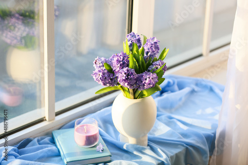 Vase with beautiful hyacinth flowers, candle and book on windowsill