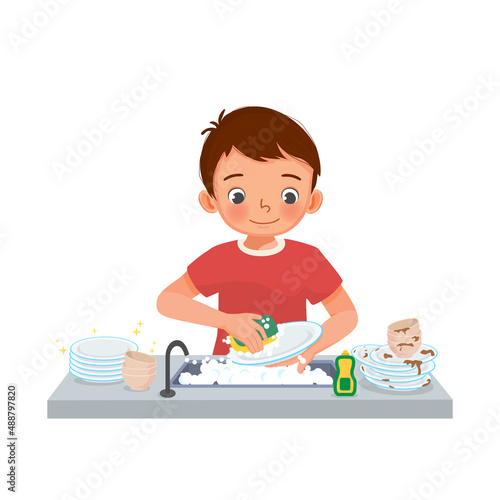 happy cute little boy washing dishes standing at sink in the kitchen doing housework chores at home