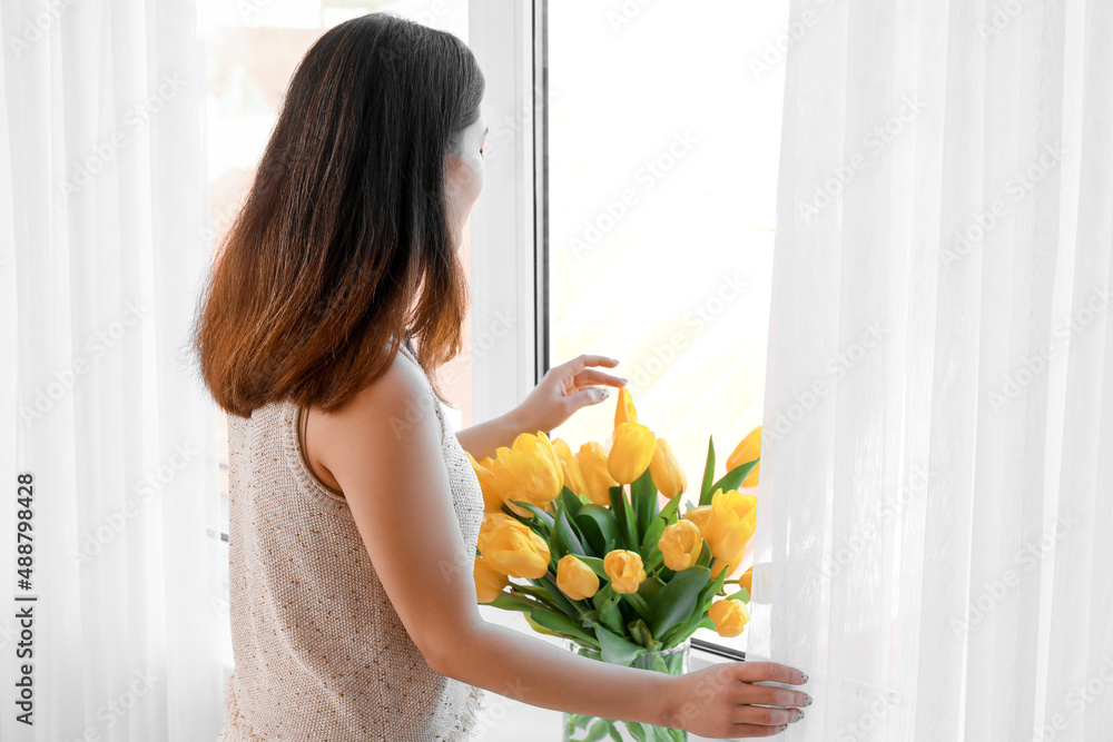 Pretty young Asian woman with flowers near window Pretty young Asian woman with flowers near window