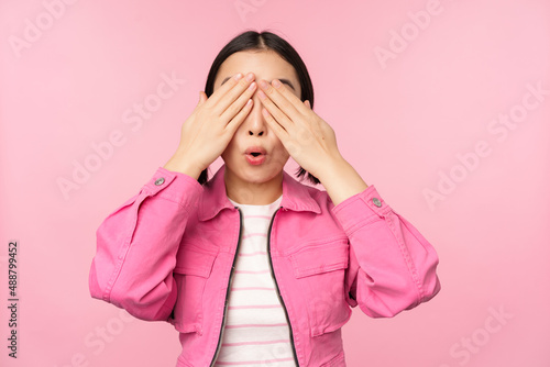 Surprise and celebration. Portrait of asian happy girl close eyes, waiting for gift, anticipating something, standing blindsided against studio background photo