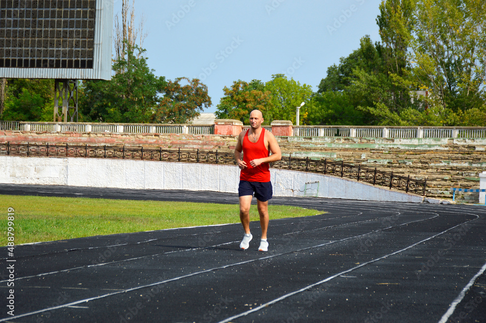 young male athlete in a red jersey conducts a running training at the stadium. man running on black rubber track outdoors young male athlete in a red jersey conducts a running training at the stadium. man running on black rubber track outdoors