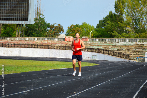young male athlete in a red jersey conducts a running training at the stadium. man running on black rubber track outdoors