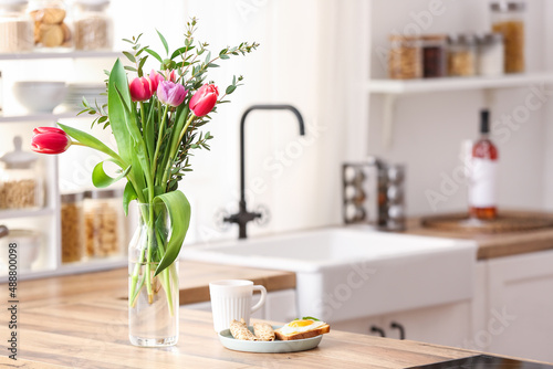 Vase with flowers and breakfast on wooden kitchen counter