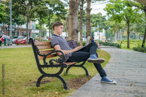 Young caucasian man sitting on the bench and working on the laptop. © Aleksandr