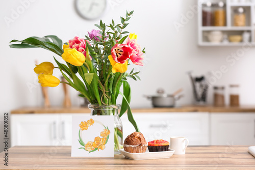 Vase with flowers, breakfast and greeting card on dining table in kitchen