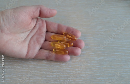 In a woman's hand are vitamins in yellow capsules.	