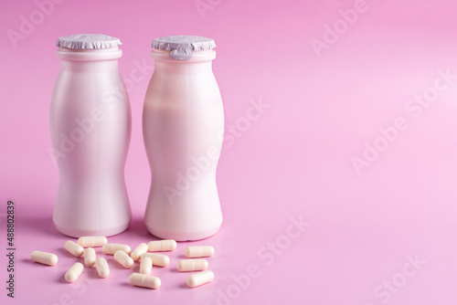 Two bottles of milk yogurt (kefir) and capsules with probiotic on a pink background. The concept of an alternative to pills and a healthy diet. Space for text.