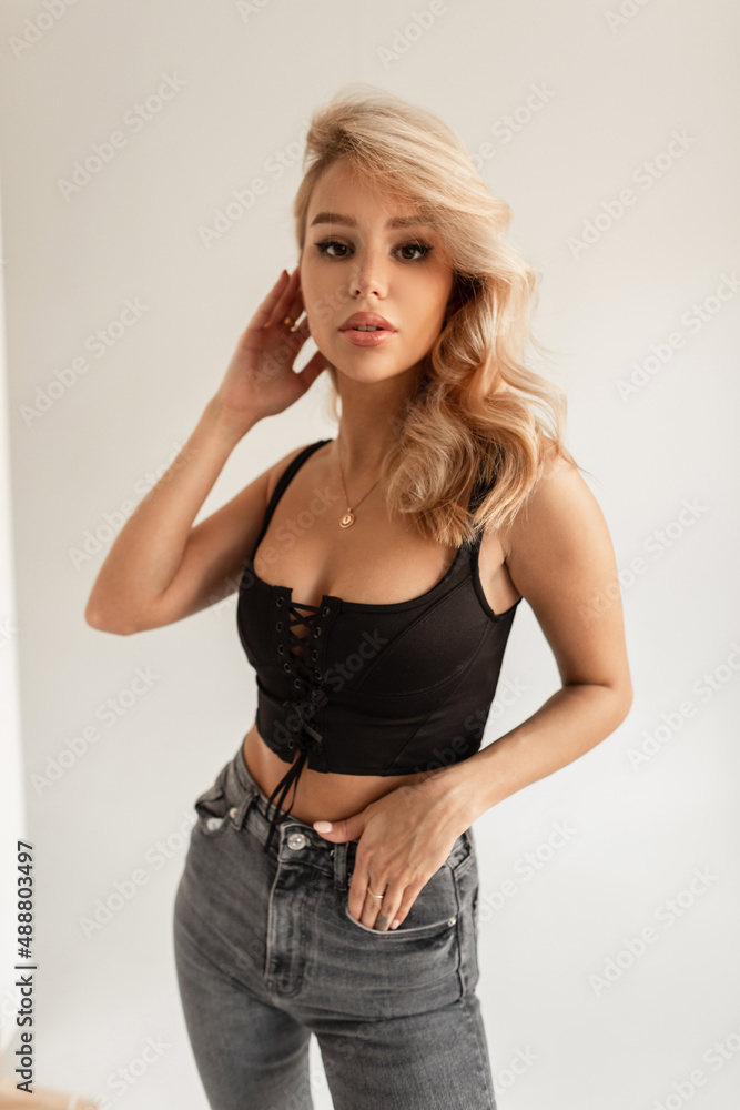 Stylish beautiful young sexy lady with blond hair in a fashion black t-shirt and vintage jeans on a white background in the studio Stylish beautiful young sexy lady with blond hair in a fashion black t-shirt and vintage jeans on a white background in the studio