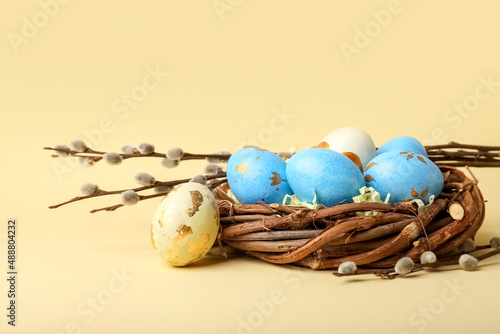Willow branches and nest with painted Easter eggs on yellow background