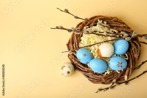 Willow branches and nest with painted Easter eggs on yellow background photo