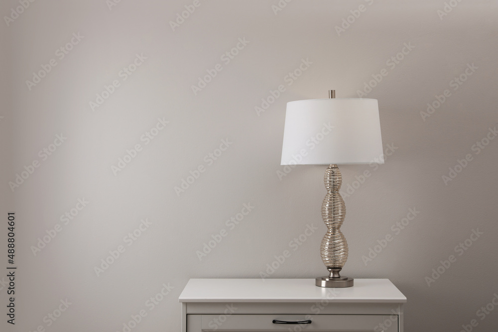 Wooden nightstand with lamp near white wall in room, space for text Wooden nightstand with lamp near white wall in room, space for text