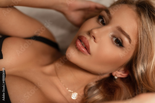 Close-up portrait of blond pretty woman with cute face and big lips lies on the bed