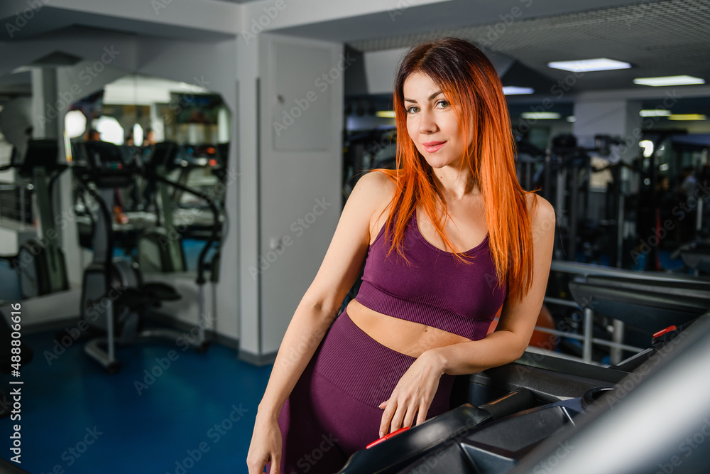Portrait of sportive fit woman in gym interior, beautiful healthy female posing at modern sports hall with equipment