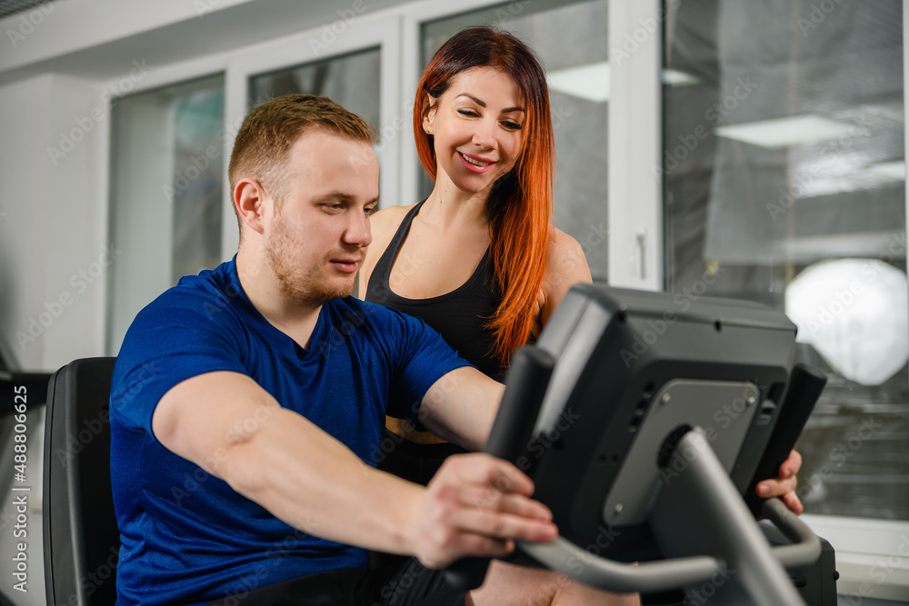 Trainer teach woman to use equipment machines at modern gym, look at screen together, start workout training exercises Trainer teach woman to use equipment machines at modern gym, look at screen together, start workout training exercises