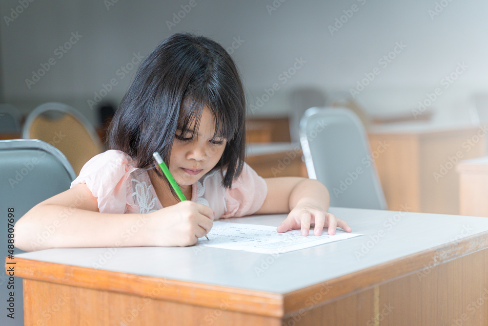 A female Asian kid student concentrate writing on the examination paper in the class A female Asian kid student concentrate writing on the examination paper in the class