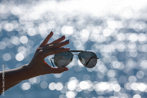 Sonnenbrille in einer Frauenhand vor unscharfen Hintergrund mit Bokeh Reflexen