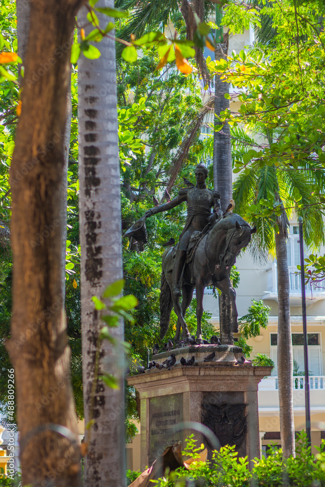 a historical monumental monument of gray color made of bronze, a rider on a horse, Bolivar, against the background of palm trees on a hot day in the tropical country of Colombia, Cartagena