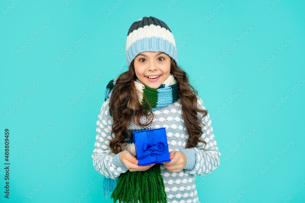 positive child in knitwear hold box. kid with present. teen girl on blue background. winter holidays