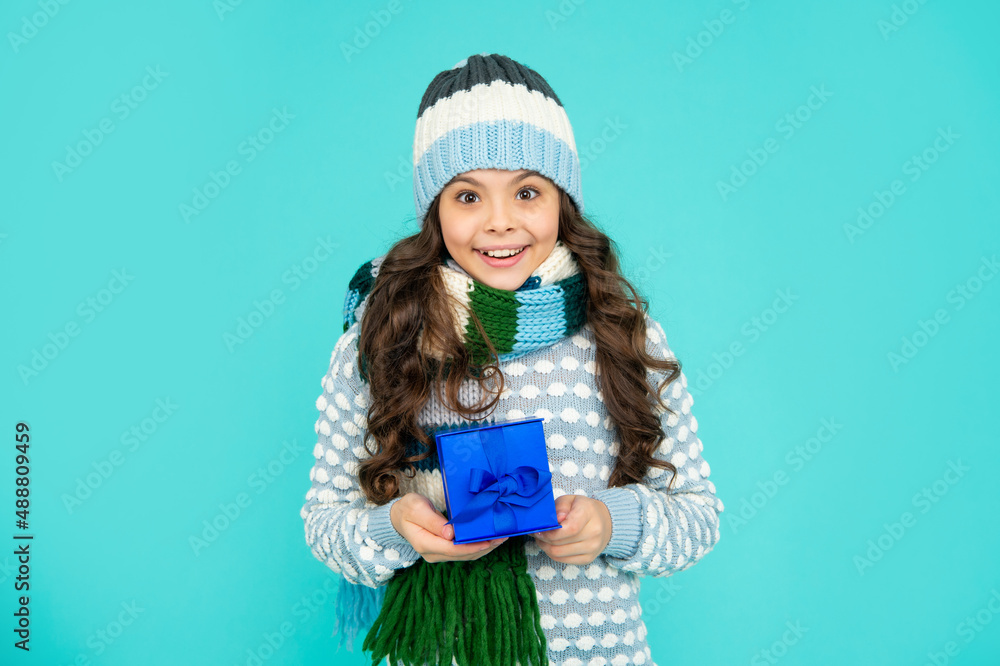 positive child in knitwear hold box. kid with present. teen girl on blue background. winter holidays positive child in knitwear hold box. kid with present. teen girl on blue background. winter holidays