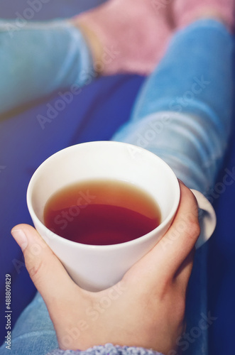 Close-up of a glass of tea in the hands of a girl in blue jeans. Vertical photography.