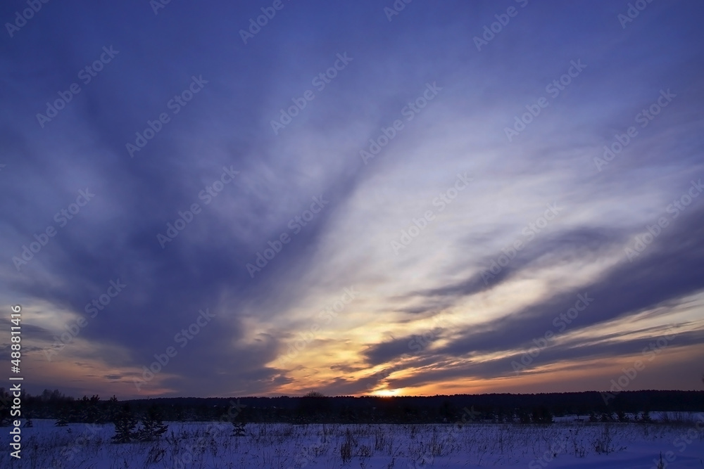 Cloudy winter sunset over snowy ground.