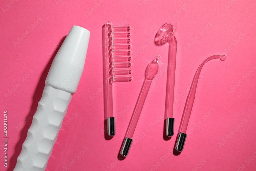 Modern darsonval with different nozzles on pink background, flat lay. Microcurrent therapy Modern darsonval with different nozzles on pink background, flat lay. Microcurrent therapy