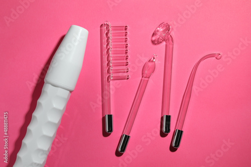 Modern darsonval with different nozzles on pink background, flat lay. Microcurrent therapy