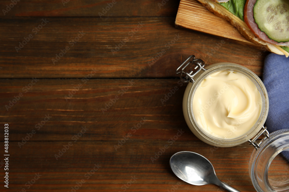 Jar of delicious mayonnaise near fresh sandwich on wooden table, flat lay. Space for text Jar of delicious mayonnaise near fresh sandwich on wooden table, flat lay. Space for text