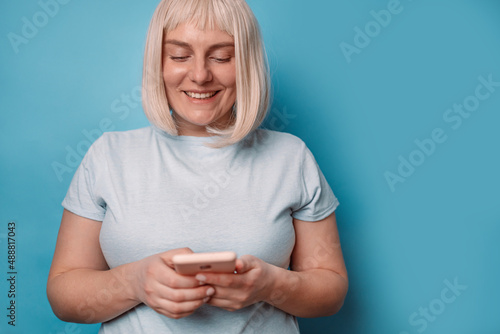 Portrait of attractive caucasian in blue t-shirt using smartphone, watching video on mobile phone isolated over blue background.