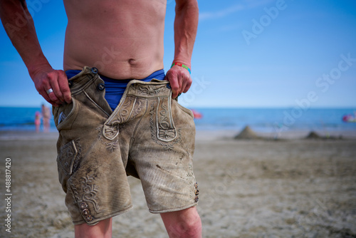 Schlanker Mann zieht sich eine Lederhose am Meer an photo