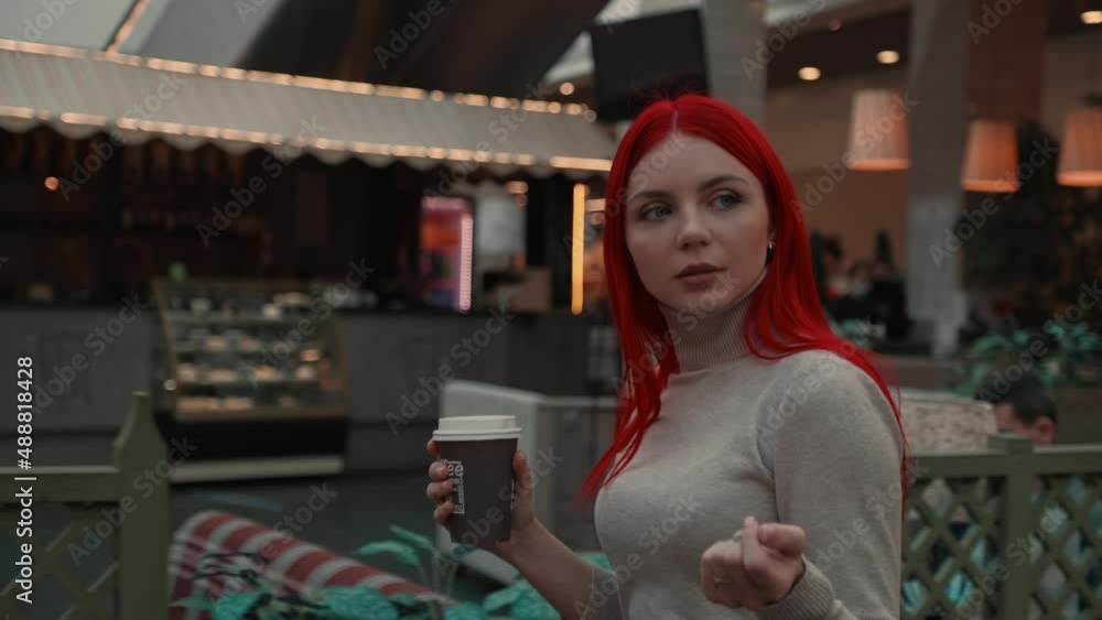 A girl with red hair walks through the mall with coffee A girl with red hair walks through the mall with coffee