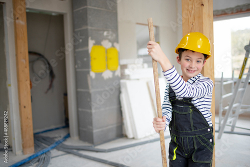 cool boy with yellow helmet posing on construction site in a house with broom