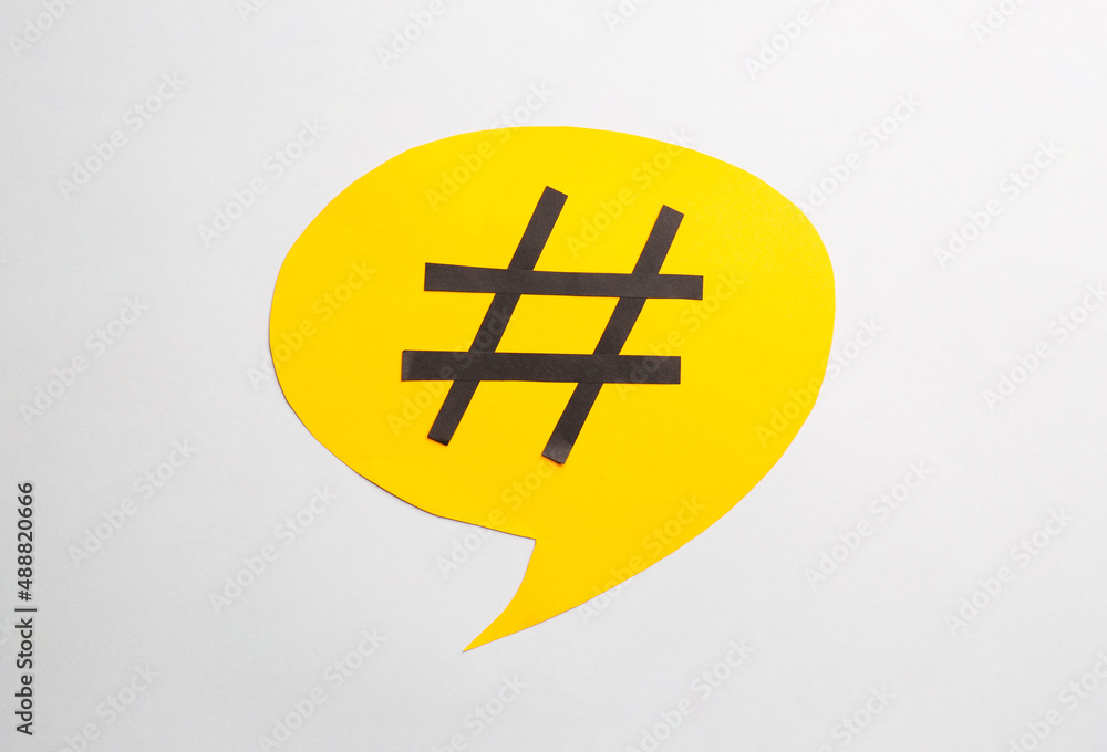 Obraz premium Yellow paper speech bubble with hashtag symbol on white background, top view