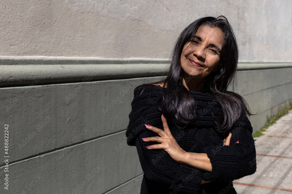 Latin American adult woman (50) poses standing in front of camera with her arms crossed, her attitude is positive. Lifestyle concept. Latin American adult woman (50) poses standing in front of camera with her arms crossed, her attitude is positive. Lifestyle concept.