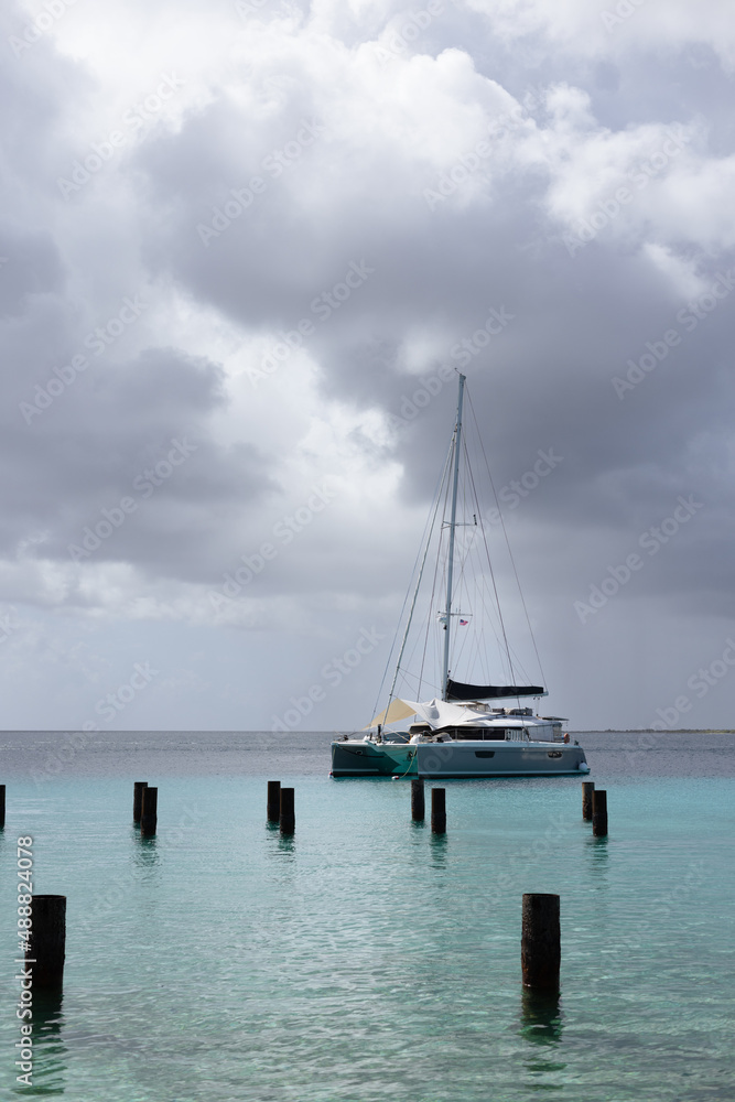 Sailboat in a harbour on azure sea under grey sky. 
