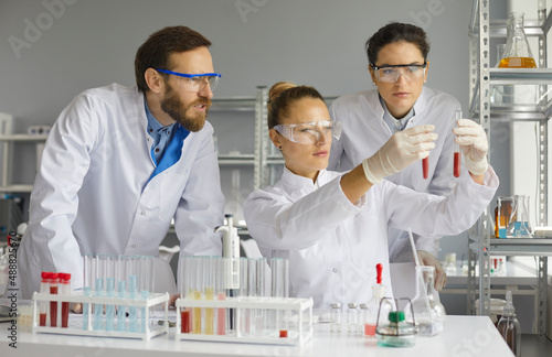 Team of scientists carefully looks at and compares blood samples in test tubes in the laboratory. Men and women work together with biological materials to develop effective drugs.