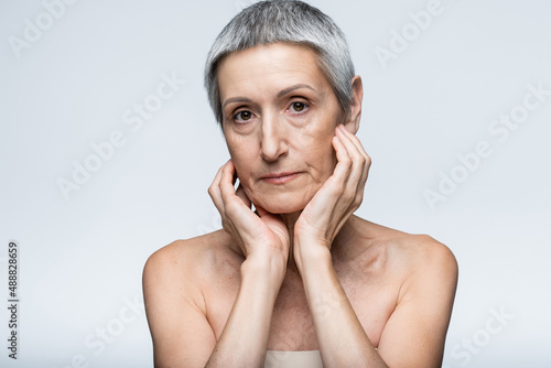 Cuadro en lienzo mature woman with bare shoulders touching cheeks and looking at camera isolated