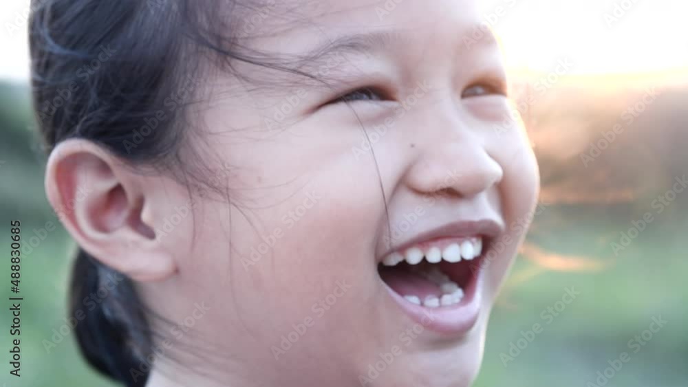 Portrait happy Asian little child girl smiling, laughing, looking at camera with beautiful sunset or sunrise in summer or spring nature outdoor background. Concept of portrait, happy children, family. Portrait happy Asian little child girl smiling, laughing, looking at camera with beautiful sunset or sunrise in summer or spring nature outdoor background. Concept of portrait, happy children, family.