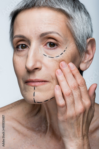 close up of mature woman with wrinkles and marked lines on face looking at camera isolated on grey