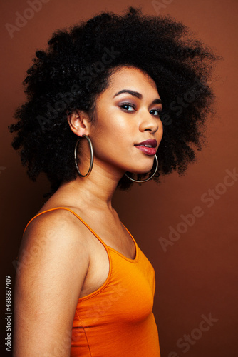 pretty young african american woman with curly hair posing cheerful gesturing on brown background  lifestyle people concept