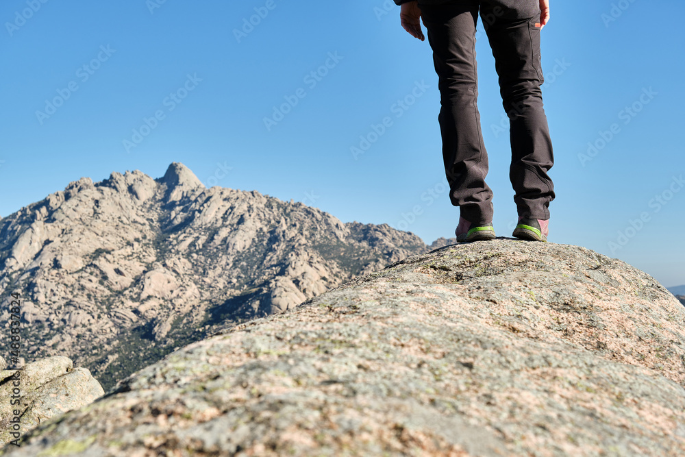 Legs of woman hiker standing on a rock contemplating the mountains.